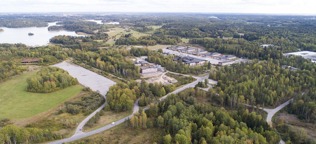 flygbild över området i Stockholm syd som visar industribyggnader, träd och fält.